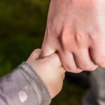 A close-up of a child and parent holding hands in a park, symbolizing love and trust.